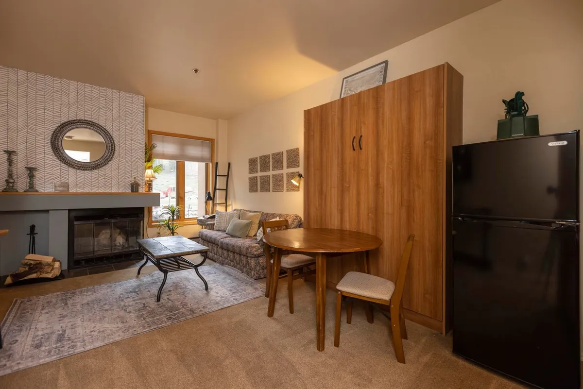 An intimate, warmly lit living space where a fireplace and a comfortable sofa take center stage. The scene also includes a dining table, all oriented to create a cozy, inviting space ideal for relaxed evenings. The overall mood encourages peaceful moments, whether by the fire or during a quiet meal.