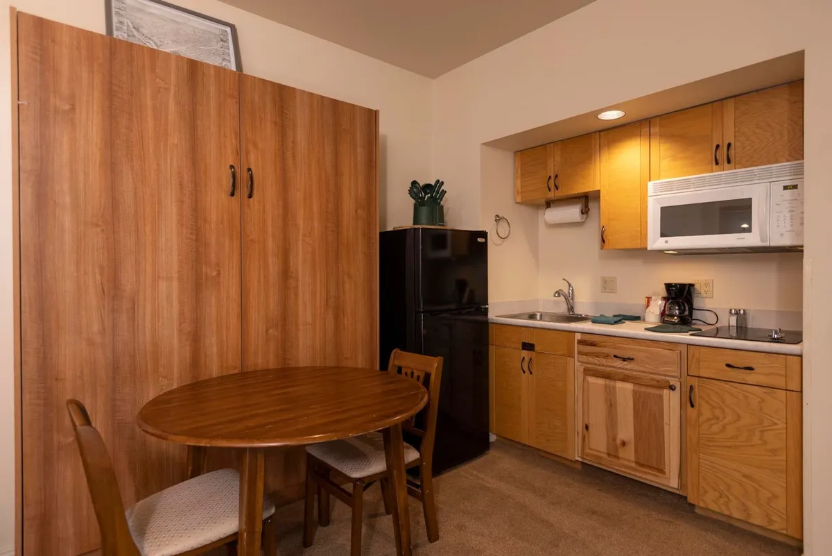 The image highlights a practical, inviting dining space with a dining table set near modern kitchen appliances and a folding cabinet. The layout encourages easy movement between meal prep and dining, creating a social and functional space for sharing food and conversation.