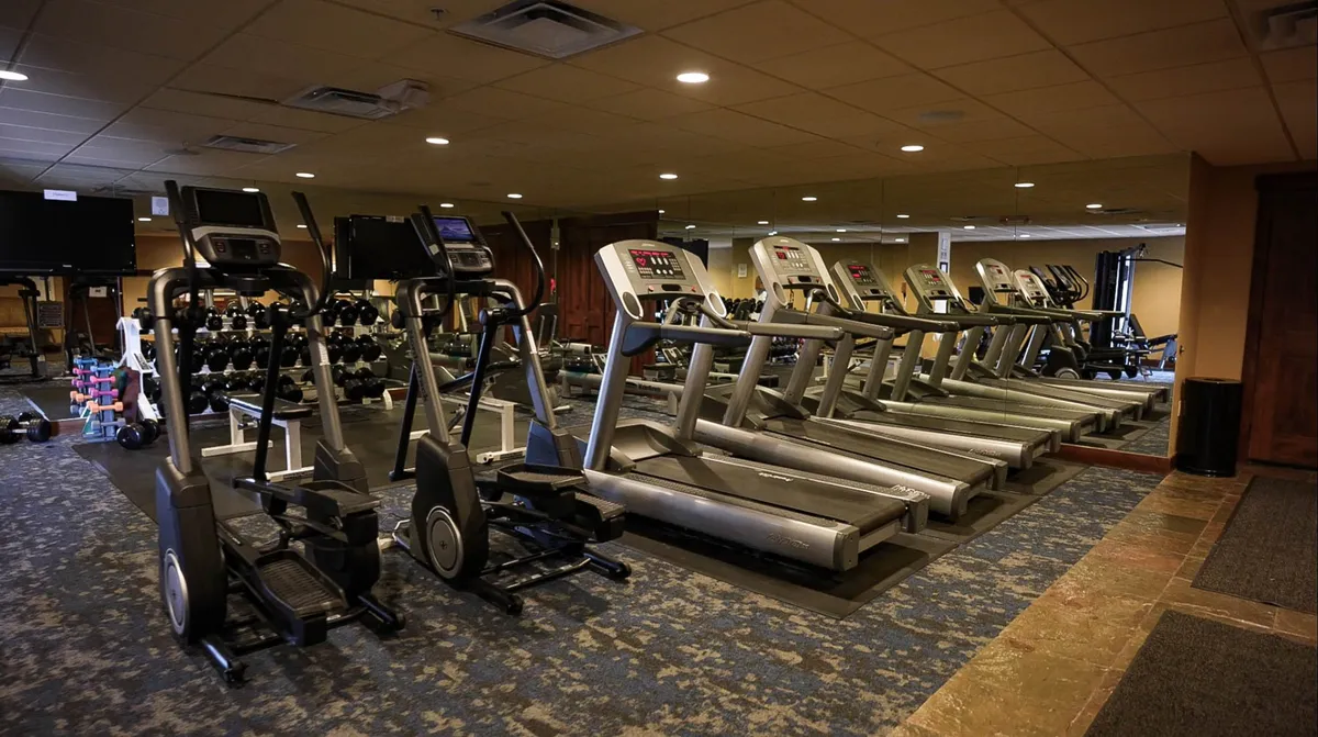 An interior fitness center equipped with treadmills, ellipticals, free weights, and mirrors. The space feels energetic and motivational, catering to guests seeking to maintain their routines or engage in active pursuits during their stay.